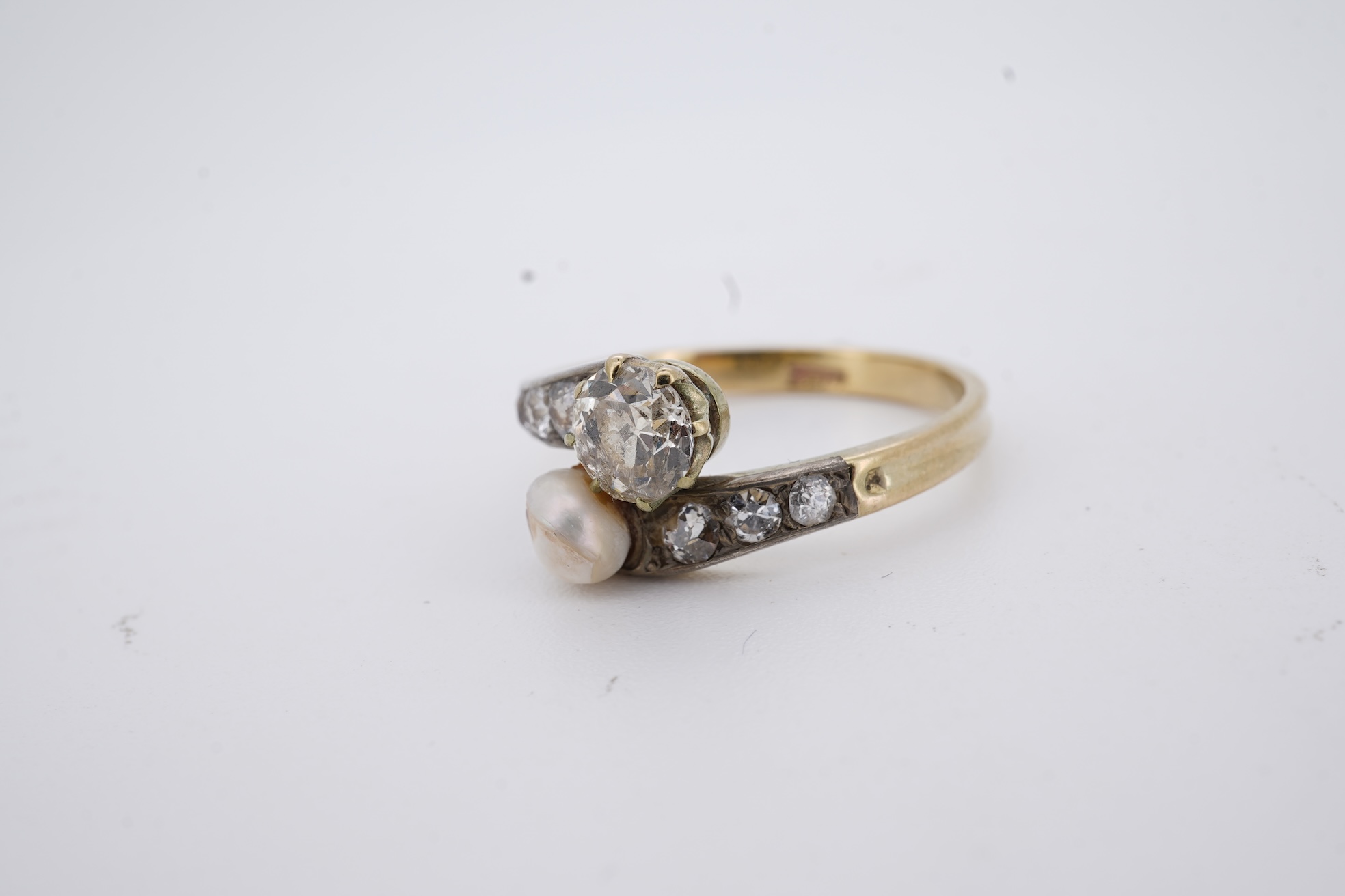 A yellow meta (stamped 18ct) cultured pearl and diamond set crossover ring, with six stone graduated diamond set shoulders, size M, gross weight 2.6 grams (pearl nacre a.f.).